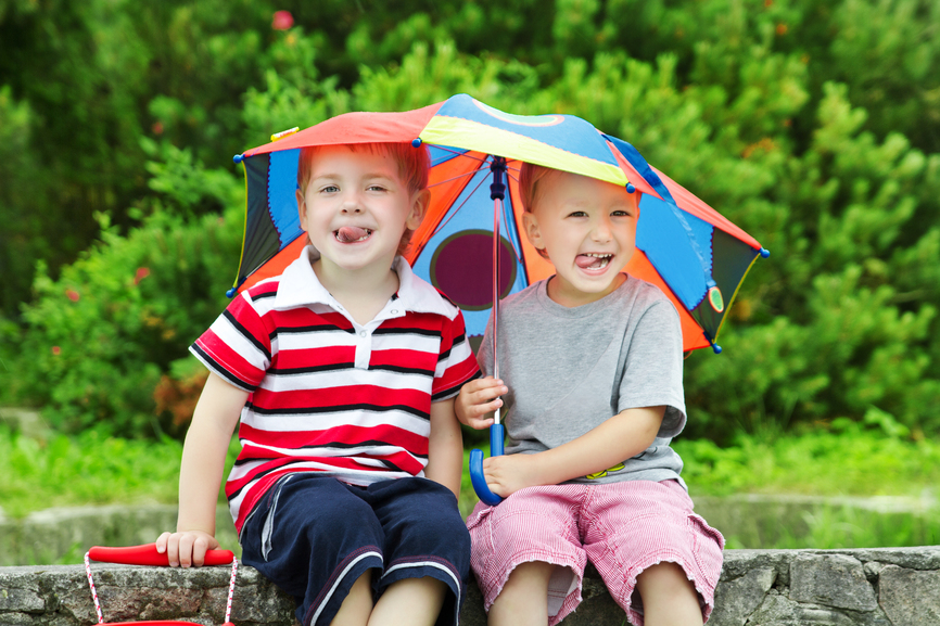 Two funny kids friends sitting under umbrella outdoor. Summer, spring season